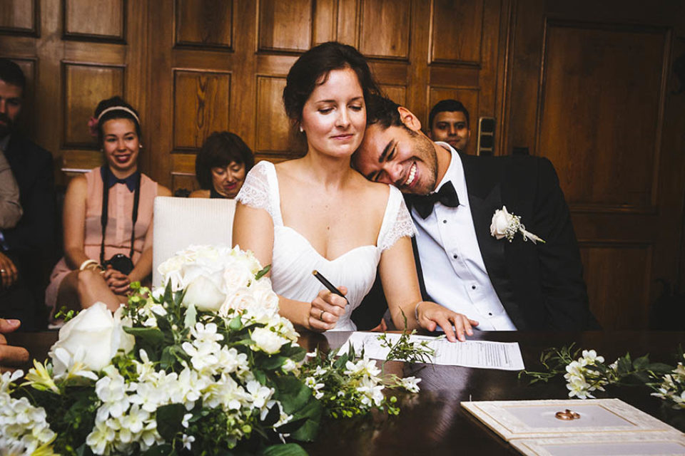 Groom laughing as bride signs wedding certificate