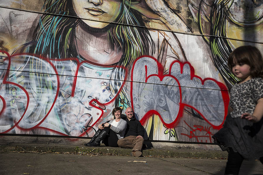 Montreal Family Photographer - Young girl running past parents by graffiti