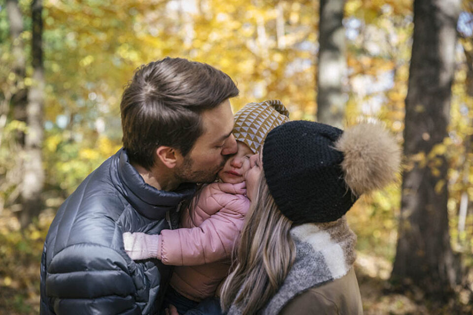 Mother and father kissing daughter