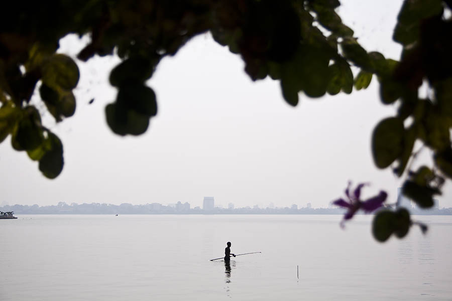A fisherman wades through the still waters of West Lake in Hanoi, Vietnam